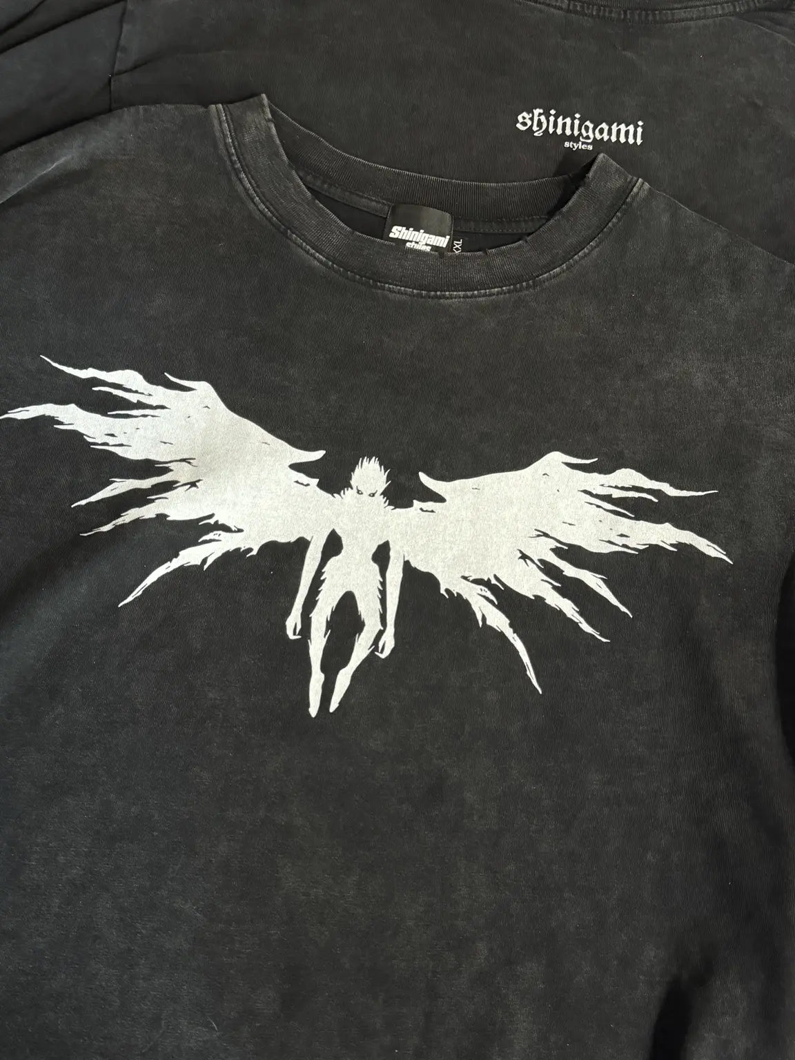 Close-up of a Shinigami Styles snow-washed tee showing the ribbed collar, neck branding, and winged graphic